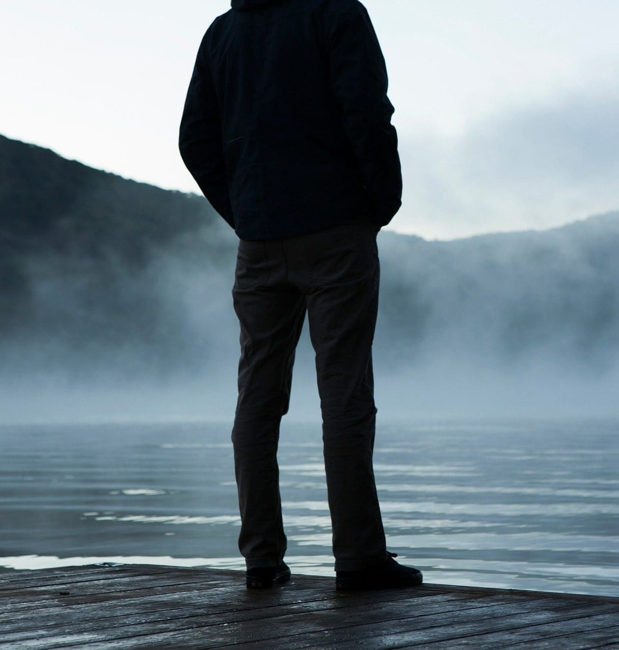 Silhouette of a man standing on a foggy dock, gazing at the mist-covered water.